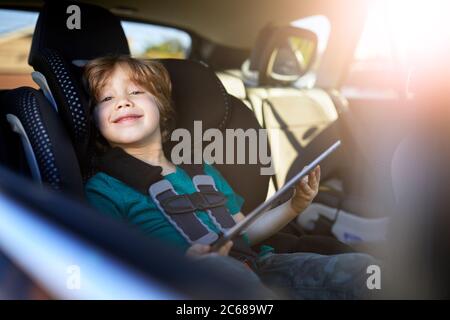 Portrait of smiling boy using digital tablet while sitting at back seat in car Stock Photo