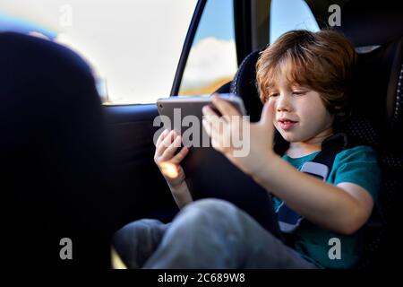 Cute boy using digital tablet while traveling in car during weekend Stock Photo