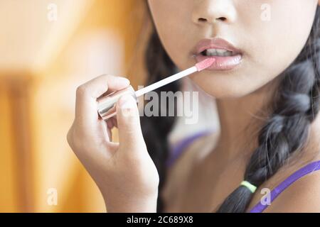 A cute long-haired Asian schoolgirl is using lipstick to apply lip makeup during a makeup lesson. Stock Photo