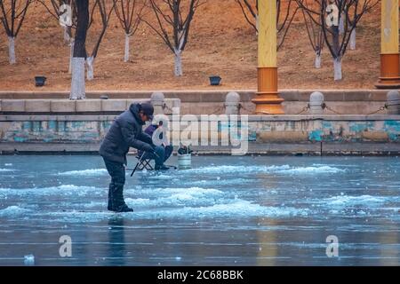 Tianjin, China - Jan 16 2020: Unidentified people ice fishing in the middle of a frosty river Haihe Stock Photo