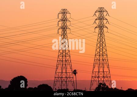 Sunset view of high voltage electricity towers on the shoreline of San Francisco bay area; California Stock Photo