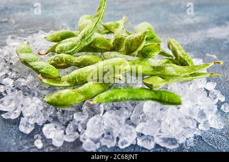 Frozen Edamame or soybeans in the mix with crushed ice on a blue background. Stock Photo