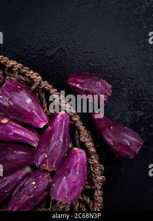 Some Barbary fig fruits in a wooden woven basket on a black background. Stock Photo