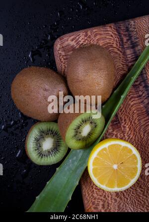 A close shot of chopped lemon, a full kiwi and an aloe vera leaf on a chopping board. Stock Photo