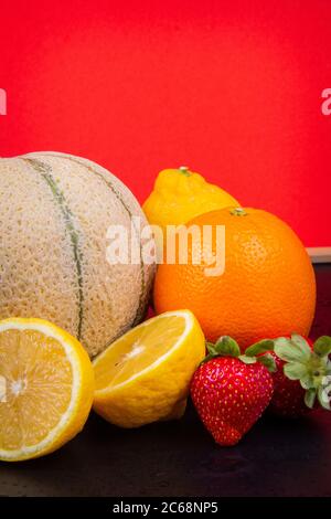 Honeydew melon, oranges, lemons and strawberries in front of a red wall. Stock Photo