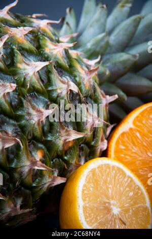 Thin slices of orange and kiwi near a big fresh pineapple on a black background. Stock Photo