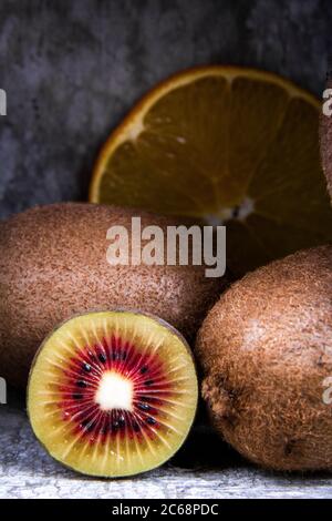 Cross sections of a red kiwi and an orange near some full kiwifruits. Stock Photo