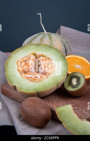 Honeydew melons, chopped kiwis and a half of a sweet orange on a wooden board. Stock Photo