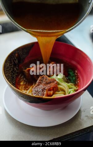 savory warm soup pouring on pork noodles in a red oriental style bowl Stock Photo