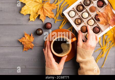 Woman's hands holding a cup of hot black coffee orange scarf box of chocolates autumn background. Top view flat layout. Stock Photo