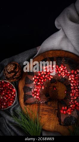 Place the chocolate cake with pomegranate seeds or slices on a wooden board with a black background. Stock Photo