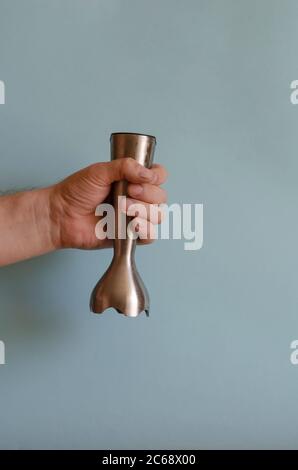 Hand holds nozzle for kitchen mixer. The left hand of a man with a metal fixture with special knives. Caucasian man 43-45 years old. Kitchen appliance Stock Photo
