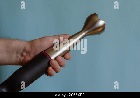 Hand holds a kitchen mixer with a nozzle. Left Hand of a man with an electric kitchen chopper. Caucasian man 43-45 years old. Kitchen appliances. Stock Photo