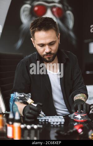 Professional tattooer in black gloves holding tattoo machine in hand preparing do tattoo in studio Stock Photo