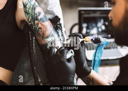 Close up professional tattoo master in black gloves doing tattoo on girl hand using tattoo machine in studio Stock Photo