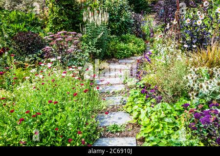A garden path between shrub and herbaceous borders in an English country garden.