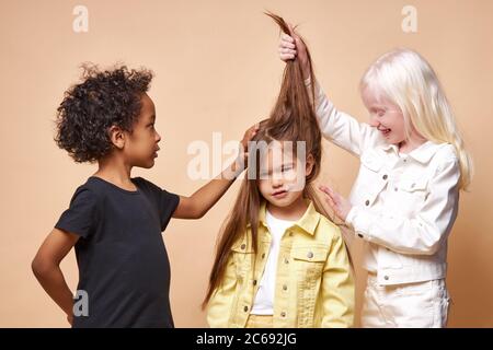 portrait of dark-skinned boy and albino girl touching caucasian friend's long hair, young hairdressers. beautiful children with unusual appearance iso Stock Photo