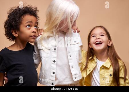 portrait of cheerful positive kids, multiethnic children isolated in studio. adorable african boy and albino, caucasian girls stand together, posing. Stock Photo