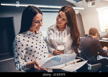 Businesswomen talking in busy meeting area of large modern office Stock Photo