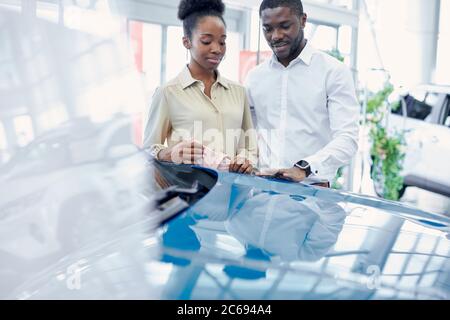 just imagine us on the road. portrait of happy african american couple checking out a car in modern dealership, they choose new car together Stock Photo