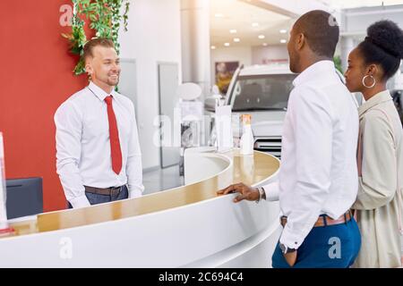 middle-aged beautiful married couple entered modern dealership, a friendly consultant meets them Stock Photo
