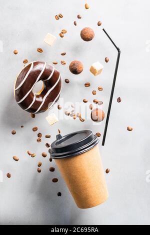 Paper cup with coffee drink or tea donut in chocolate coffee beans on a gray background. Creative fashionable levitation Stock Photo