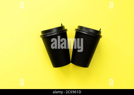 Two disposable coffee cup on yellow background. Black craft glass for coffee or tea. Stock Photo