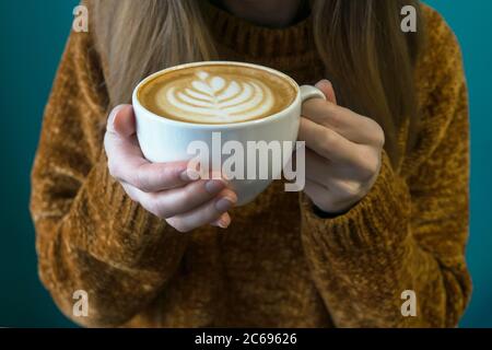 Woman in terracotta sweater headless and hands with latte. Turquoise background. Stock Photo