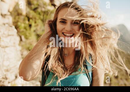 Close-up of a beautiful woman on mountain trail with her hair flying. Female mountaineer with hair flying in wind. Stock Photo