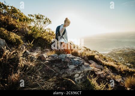Woman with backpack moving down the mountain. Female mountaineer going down the cliff. Stock Photo