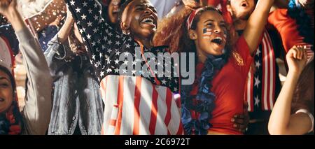 Excited fans in sports crowd, celebrating and cheering on team success. Group of American soccer fans celebrating victory. Stock Photo