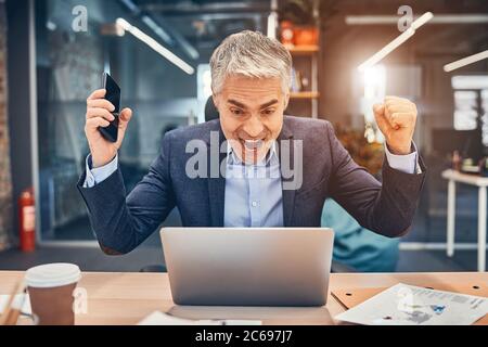 Happy businessman in suit looking at laptop excited by good news online Stock Photo