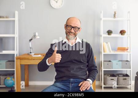 Positive senior man comminucating online, showing thumb up gesture at home. Elderly vlogger broadcasting on webcam Stock Photo