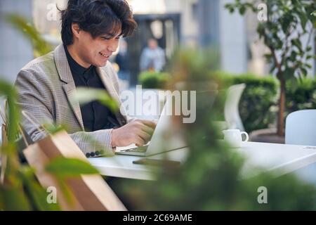 Joyful young man using notebook in outdoor cafe Stock Photo
