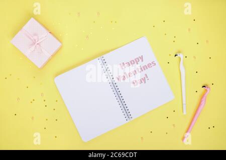Creative flat lay of bloggers workspace. Top view of notepad, pink gift box and two pens flamingo. Yellow backdrop with stars and beads. Happy Valenti Stock Photo