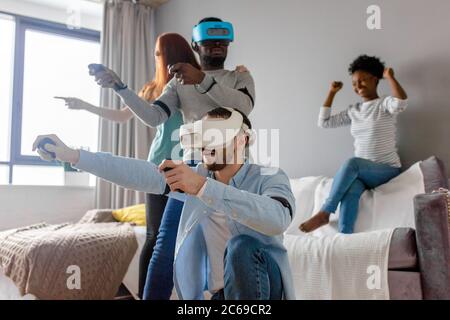 Multiethnic diverse friends enjoying VR technology, two guys wearing vr headset and playing while african and caucasian redhead girl look at them and Stock Photo