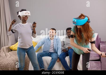 Now it is girl s turn to play 3D reality tennis game on virtual tennis court, interracial female couple female in VR headset experience exciting emoti Stock Photo