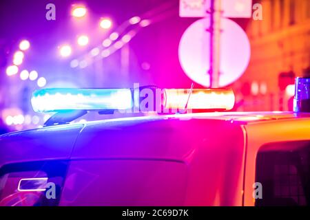 Police car in action with blinking light and siren signal at night in the city. Blurred bokeh background, public lighting lamps. Stock Photo