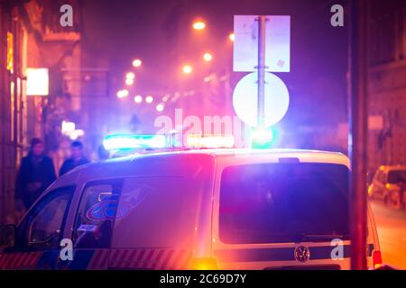 Police car in action with blinking light and siren signal at night in the city. Blurred bokeh background, public lighting lamps. Stock Photo