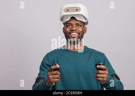 Young dark skinned guy getting excited after watching 3 D film using virtual reality headset, looking at camera isolated in green wear over grey backg Stock Photo