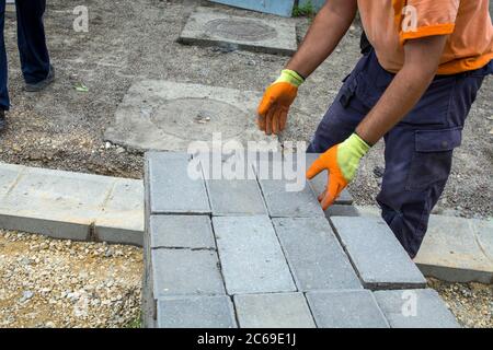 The master is laying new concrete bricks for the sidewalk on the pile. The bricks have been prepared for the laying of a new footpath. Stock Photo
