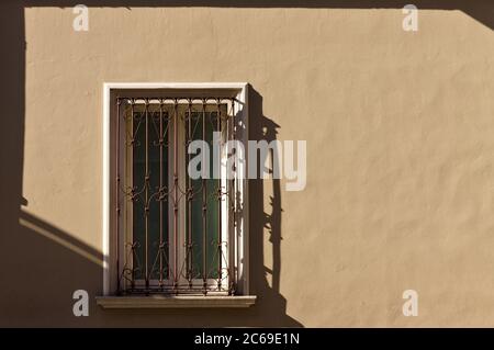 An isolated white window with rusted gratings in an ocher wall (Pesaro, Italy, Europe) Stock Photo