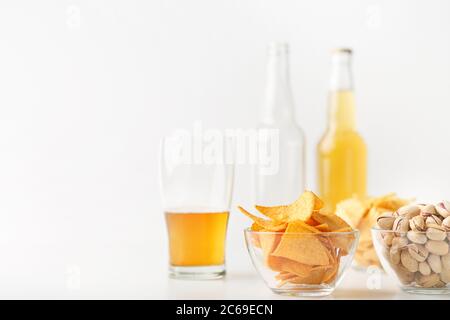 Set of snacks and beer for clients. Half glass of beer, empty and full bottle, nachos, chips and pistachios in glass plates Stock Photo