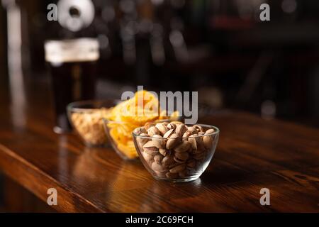 Snack to beer. Pistachios, chips and nuts in glass bowls on wooden brown bar Stock Photo