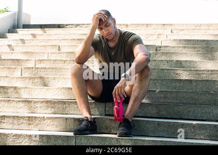 Tired black sportsman resting on stone stairs after workout outdoor Stock Photo