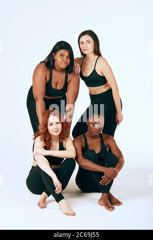 Group of four women of different race, figure type and size in sports outfit posing together over white background. Stock Photo