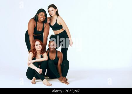 Group of women of different race, figure and size in sportswear posing together as group, looking confidently at camera against white background. Stock Photo