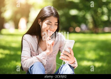 Joyful Korean Girl Having Video Call On Smartphone While Relaxing In Park Stock Photo