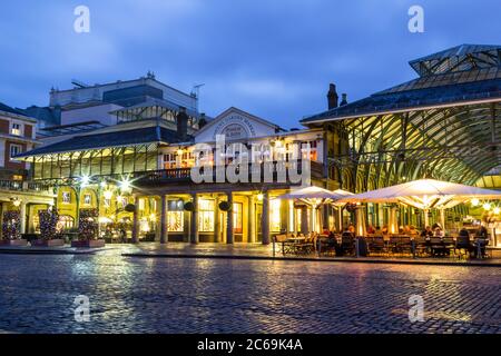 LONDON, UK - 24TH FEB 2014: Covent Garden at dusk, showing people sitting down outside and the entrances to the market Stock Photo