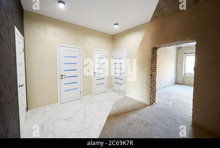 Horizontal snapshot of a room in a big apartment, before and after versions, modernized corridor with many closed white doors, spot lights on the ceiling in a light hallway Stock Photo